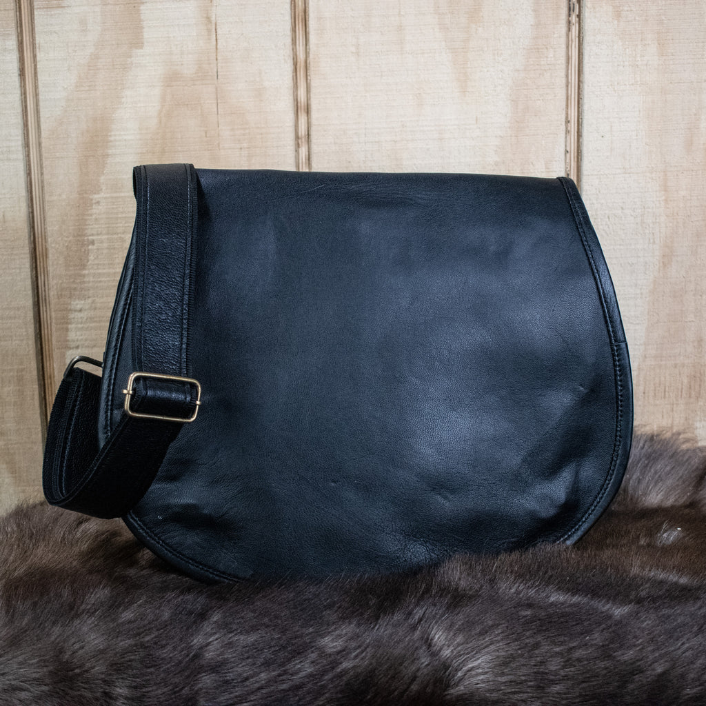A black leather satchel with a shoulder strap placed against a wooden background.