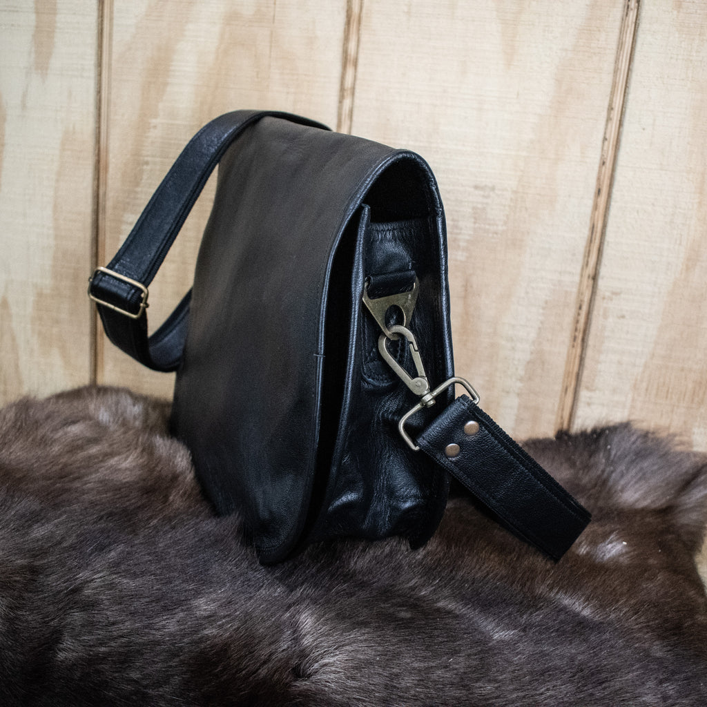 A black leather satchel with a shoulder strap placed against a wooden background.