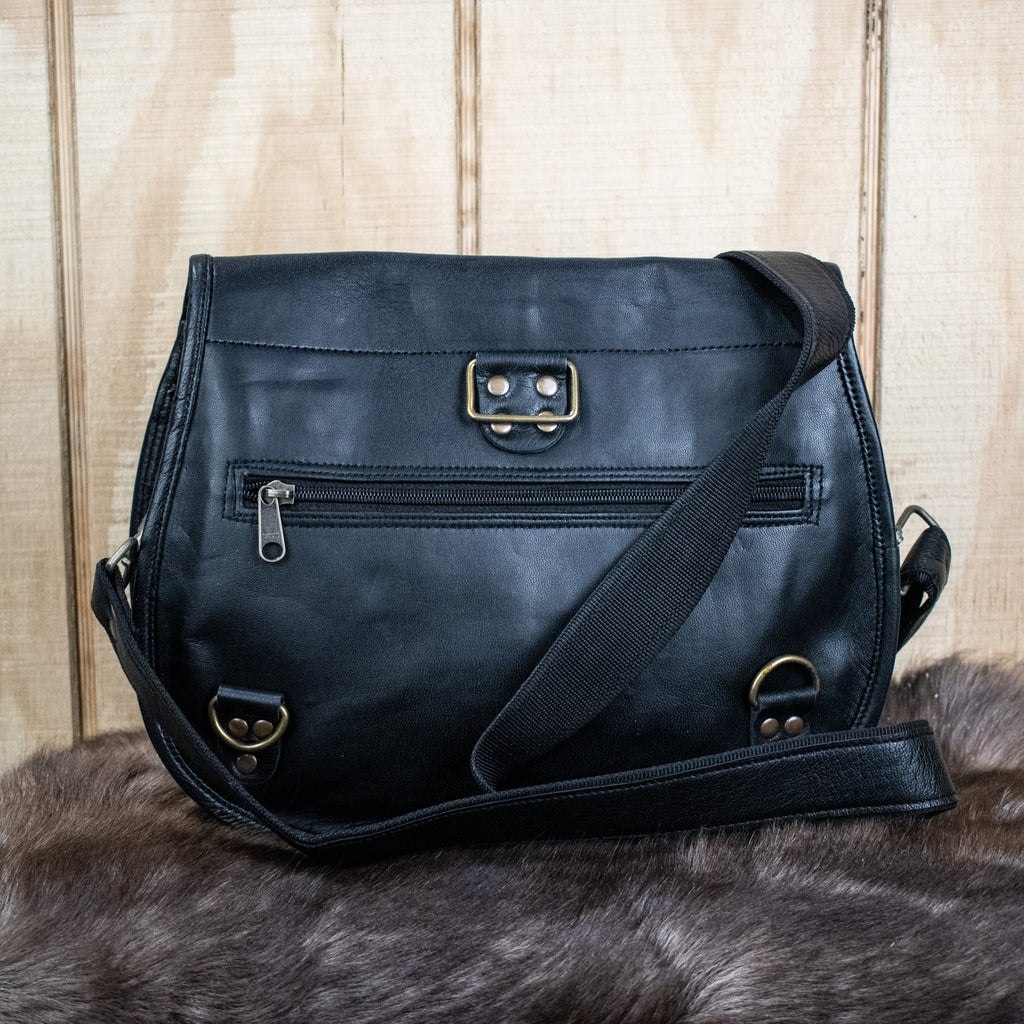 A black leather satchel with a shoulder strap placed against a wooden background.