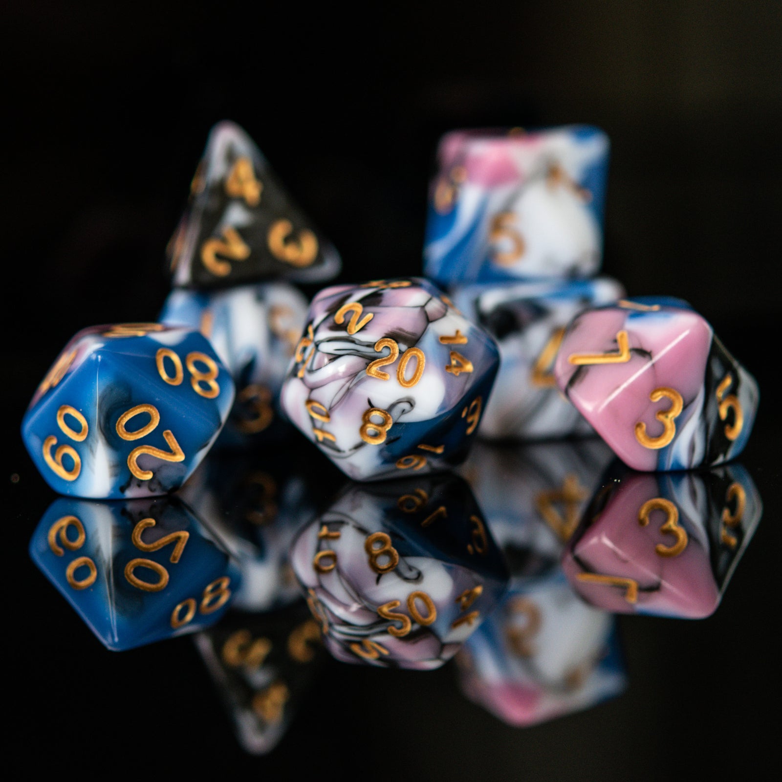 A set of acrylic dice with engraved numbers, featuring a variety of colors including blue, pink, white, and black, displayed on a reflective surface for playing tabletop games war games and board games