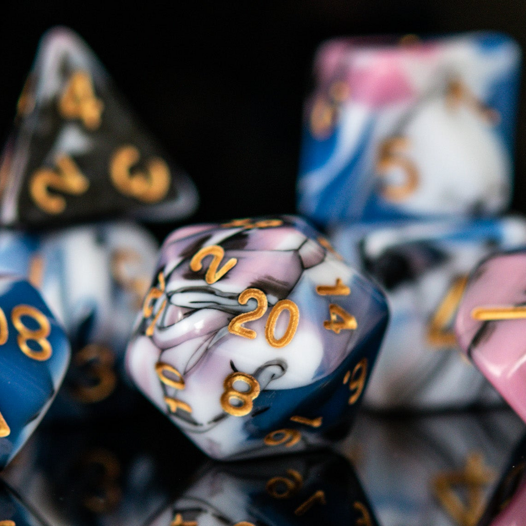 A set of acrylic dice with engraved numbers, featuring a variety of colors including blue, pink, white, and black, displayed on a reflective surface for playing tabletop games war games and board games 