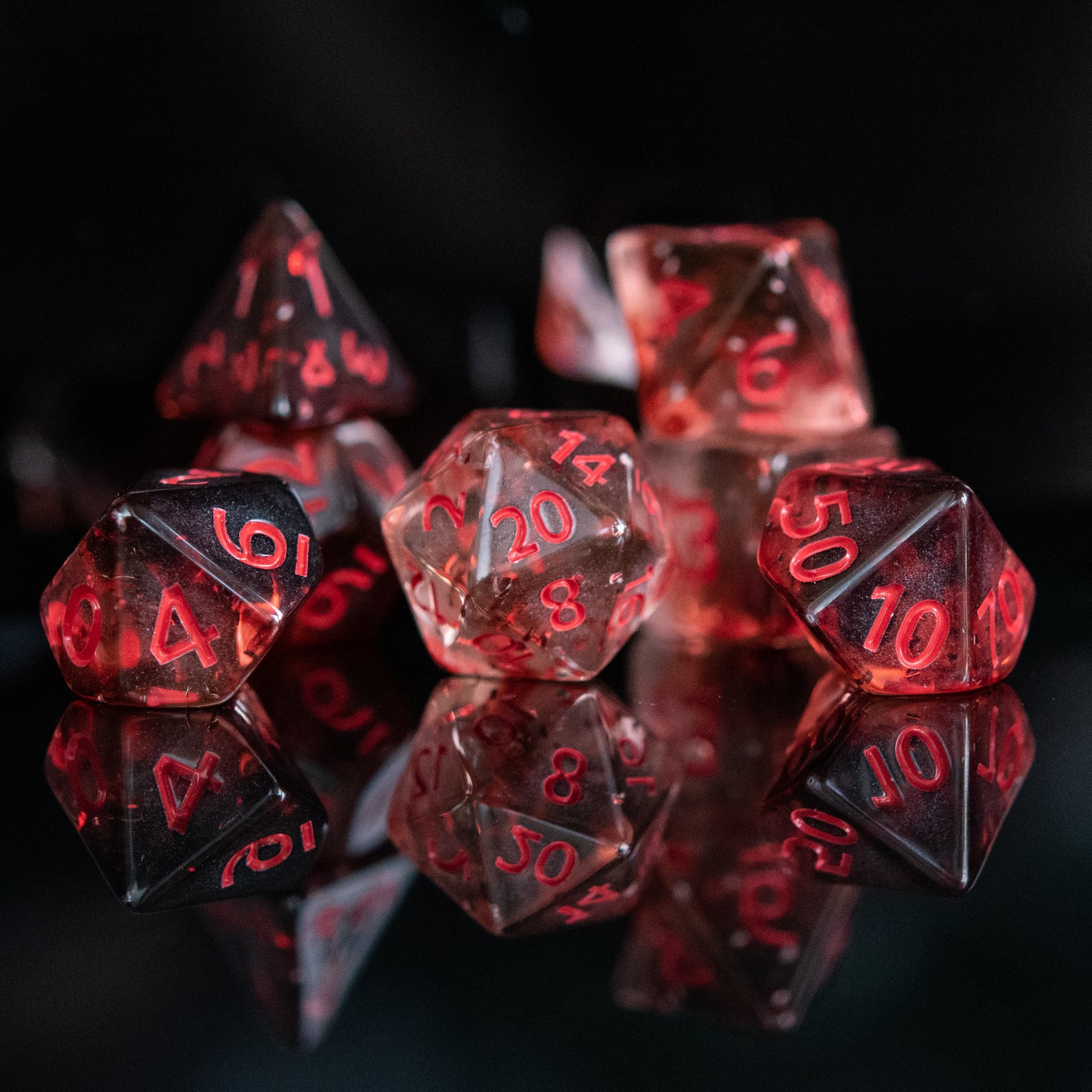 A set of acrylic dice with red numbers, including various shapes typical for role-playing games like a d4, d6, d8, d10, d12, and d20, displayed on a reflective surface.