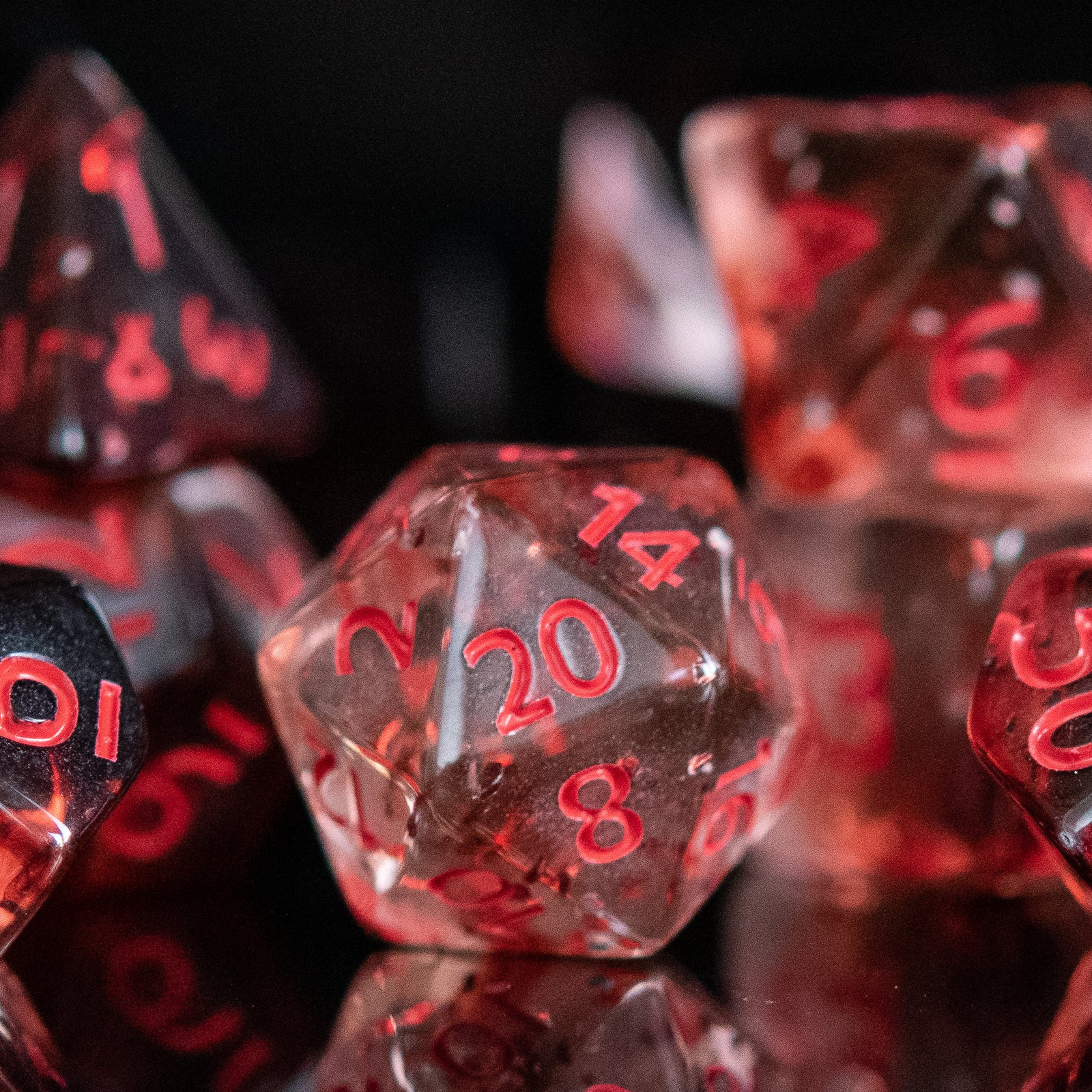 A set of acrylic dice with red numbers, including various shapes typical for role-playing games like a d4, d6, d8, d10, d12, and d20, displayed on a reflective surface.
