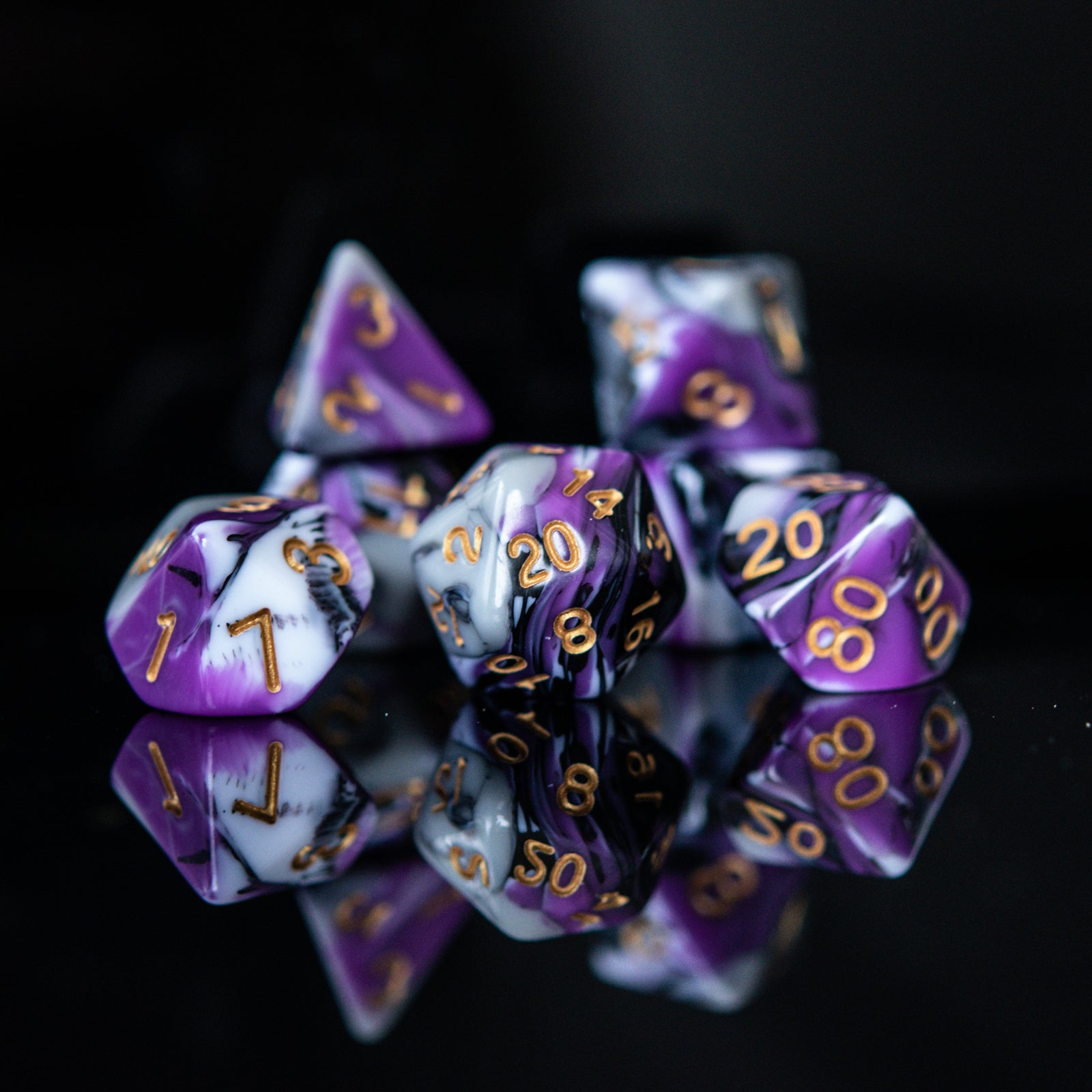 A set of acrylic dnd dice with purple, white, and black colors, featuring engraved gold numbers, arranged on a reflective surface for playing wargaming tabletop gaming and board games