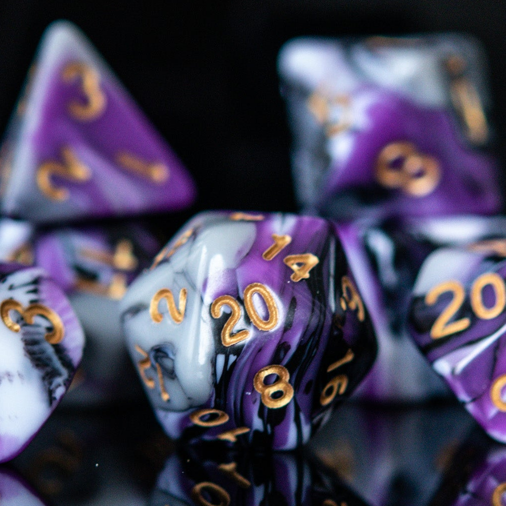 A set of acrylic dnd dice with purple, white, and black colors, featuring engraved gold numbers, arranged on a reflective surface for playing wargaming tabletop gaming and board games 