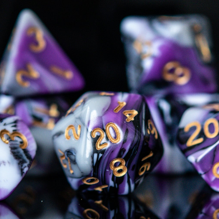 A set of acrylic dnd dice with purple, white, and black colors, featuring engraved gold numbers, arranged on a reflective surface for playing wargaming tabletop gaming and board games 