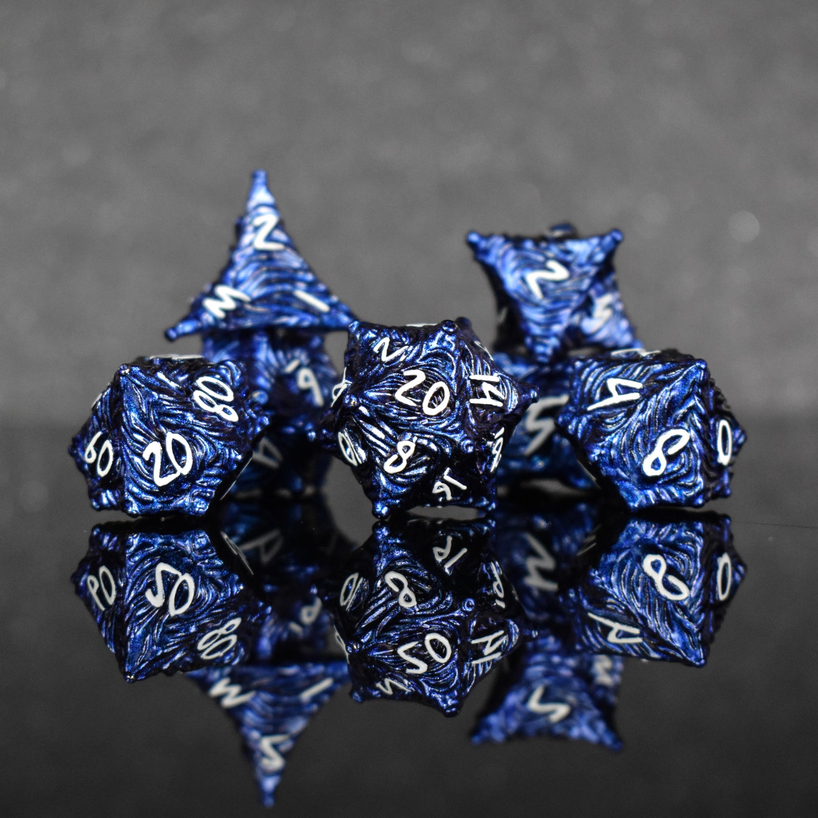 a set of dark blue metal dice with vortex swirls and a white font