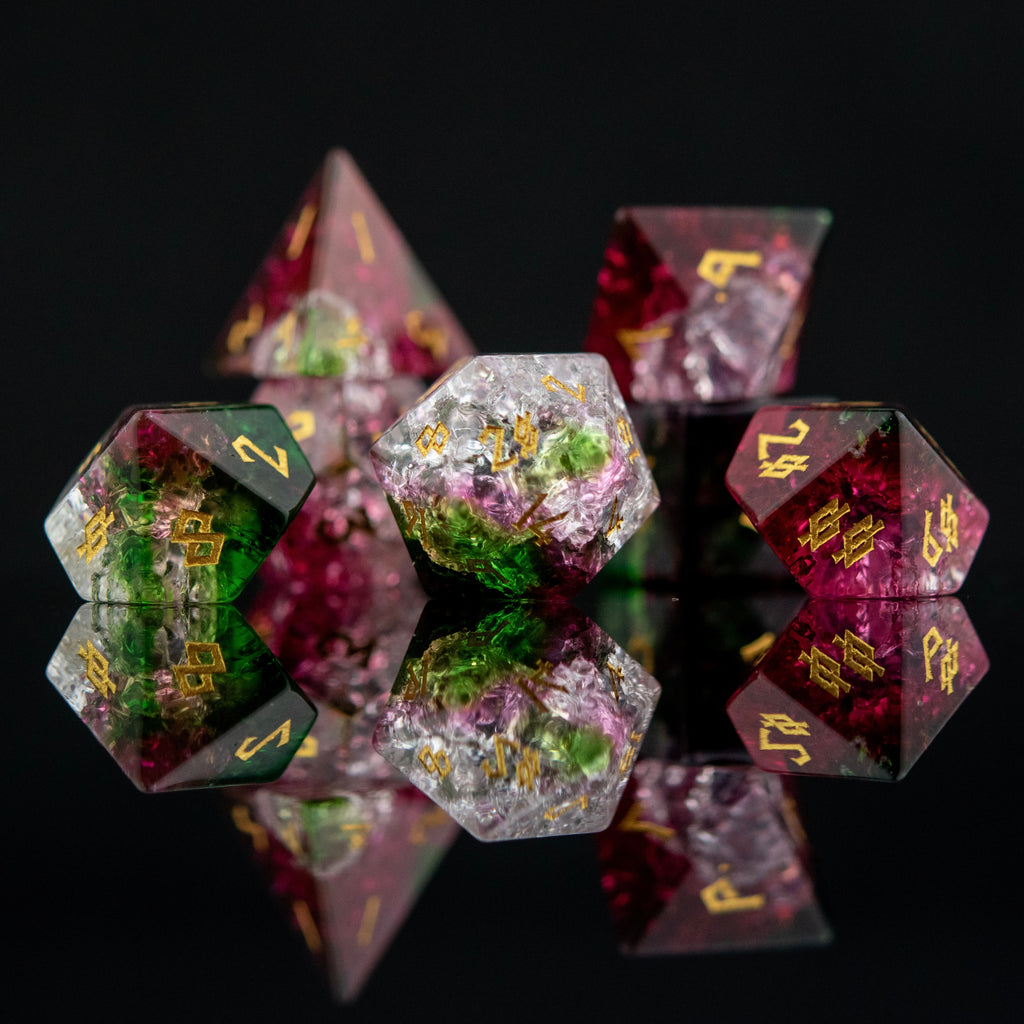 A set of hand-carved, multicolored glass dice with shattered glass effect and engraved numbers, displayed on a reflective surface.