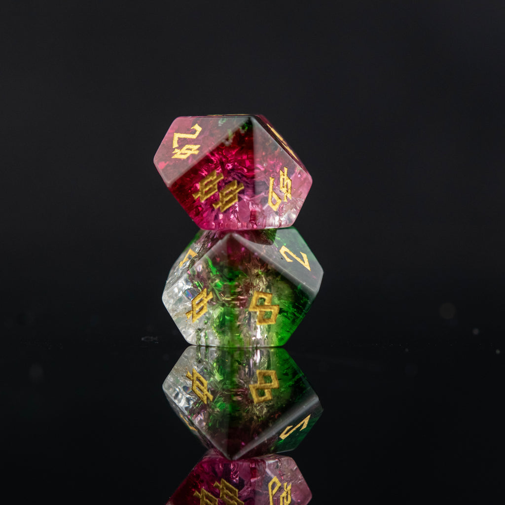 A set of hand-carved, multicolored glass dice with shattered glass effect and engraved numbers, displayed on a reflective surface.
