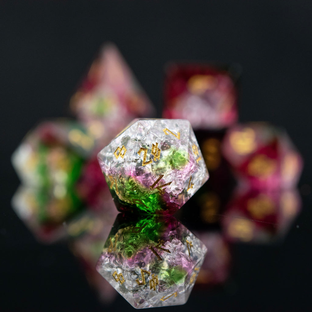 A set of hand-carved, multicolored glass dice with shattered glass effect and engraved numbers, displayed on a reflective surface.