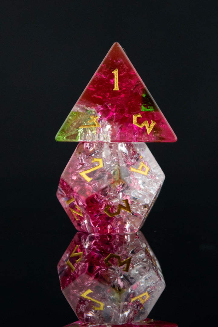A set of hand-carved, multicolored glass dice with shattered glass effect and engraved numbers, displayed on a reflective surface.