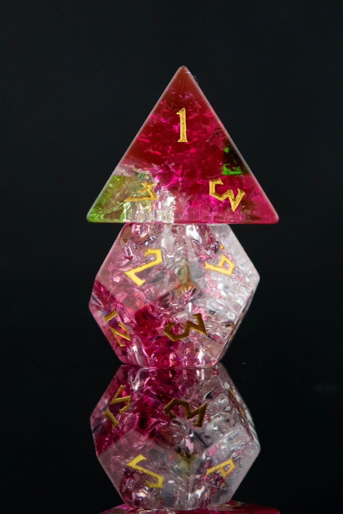 A set of hand-carved, multicolored glass dice with shattered glass effect and engraved numbers, displayed on a reflective surface.