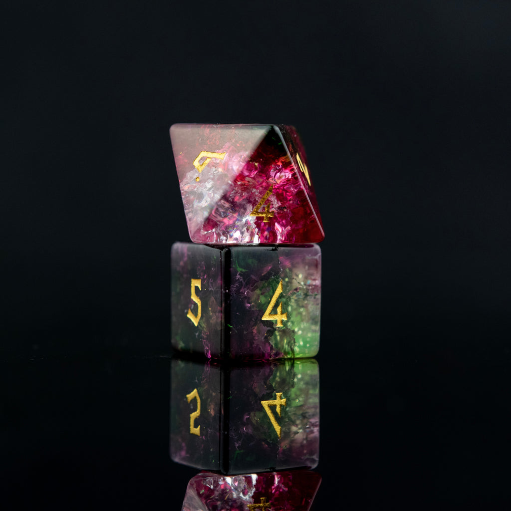 A set of hand-carved, multicolored glass dice with shattered glass effect and engraved numbers, displayed on a reflective surface.