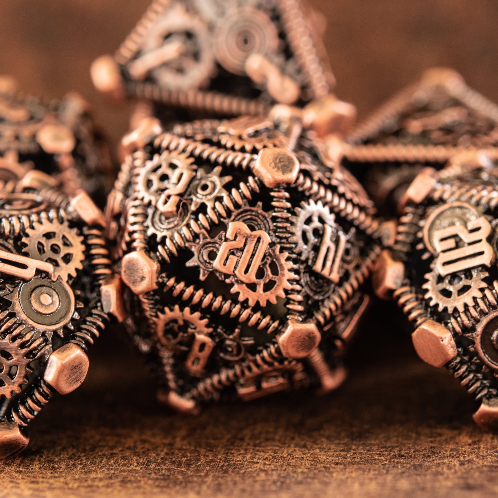 A set of bronze metal hollow dice with embossed numbers, including multiple dice types, displayed on a wooden surface.