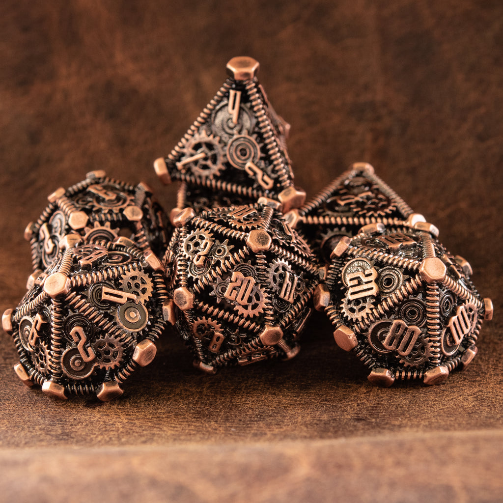 A set of bronze metal hollow dice with embossed numbers, including multiple dice types, displayed on a wooden surface.