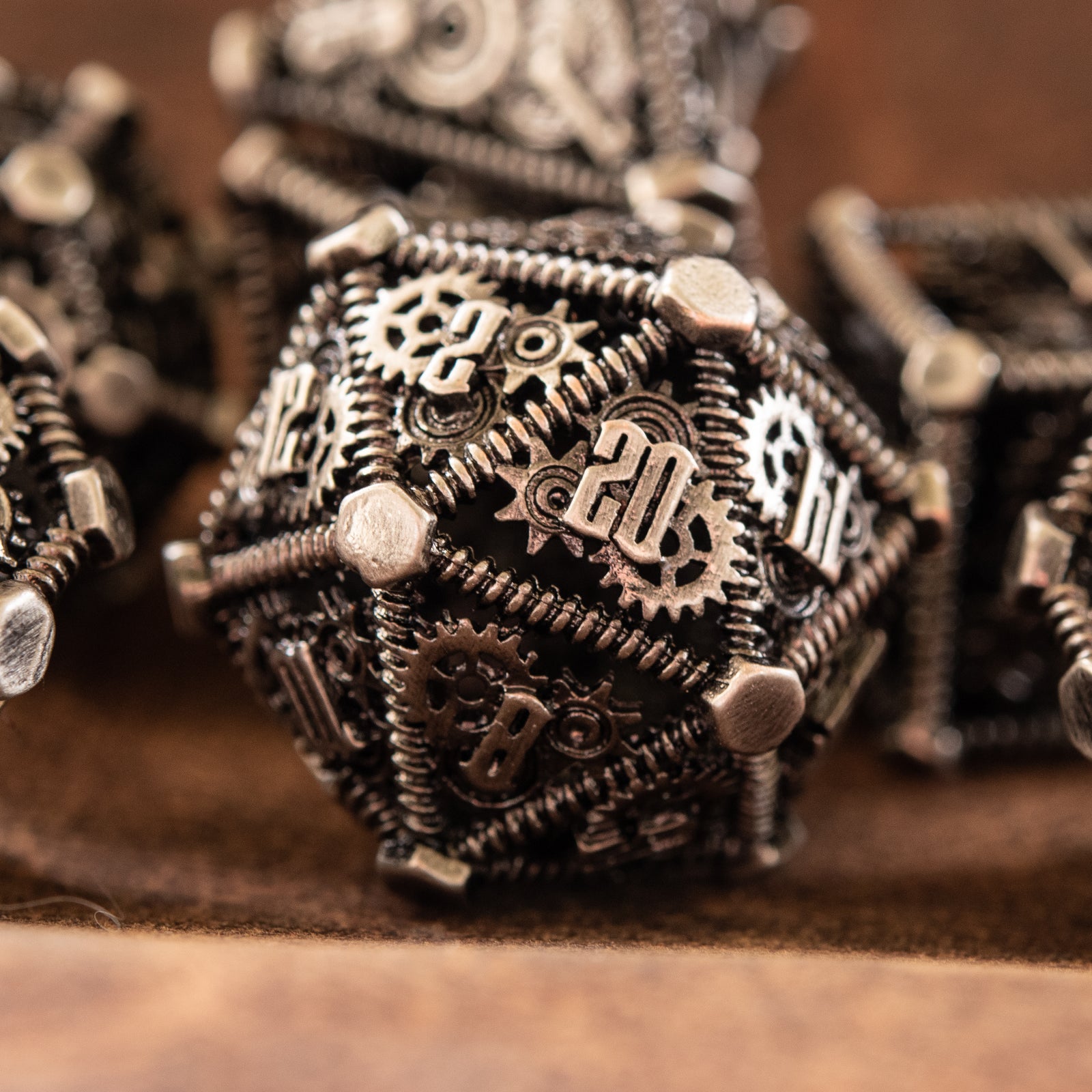 A set of silver metal hollow dice with embossed numbers, including various shapes typical for role-playing games, displayed on a textured background.