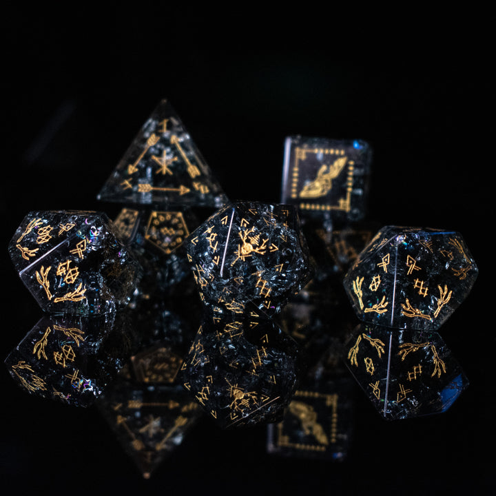 A collection of hand-carved, smoky-gray glass dice with gold engraved numbers and wendigo inspired details, displayed against a black background.