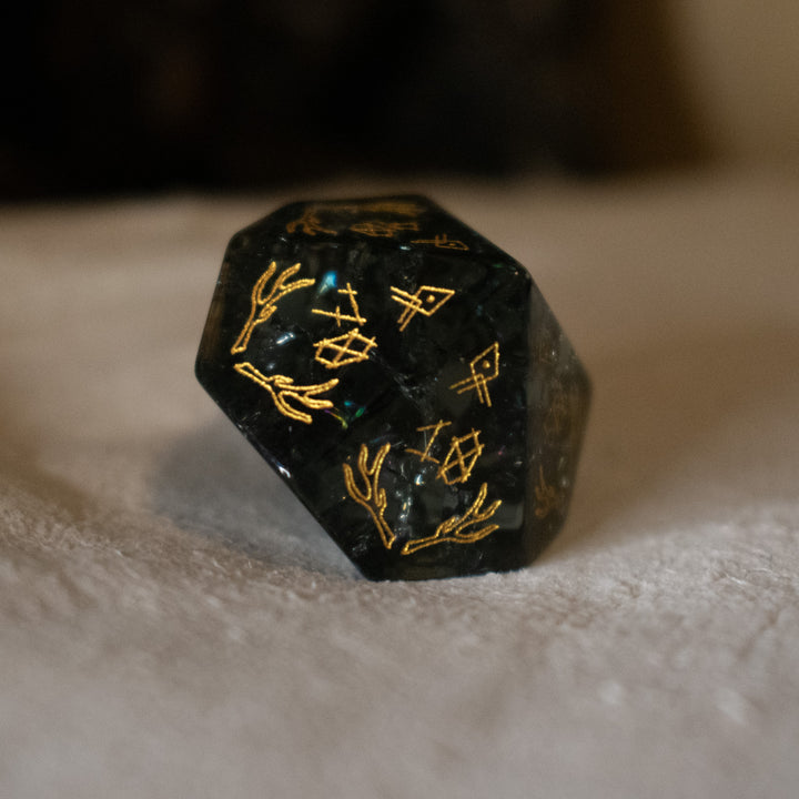 hand-carved, smoky-gray glass dice with gold engraved numbers and wendigo inspired details, displayed against a black background.