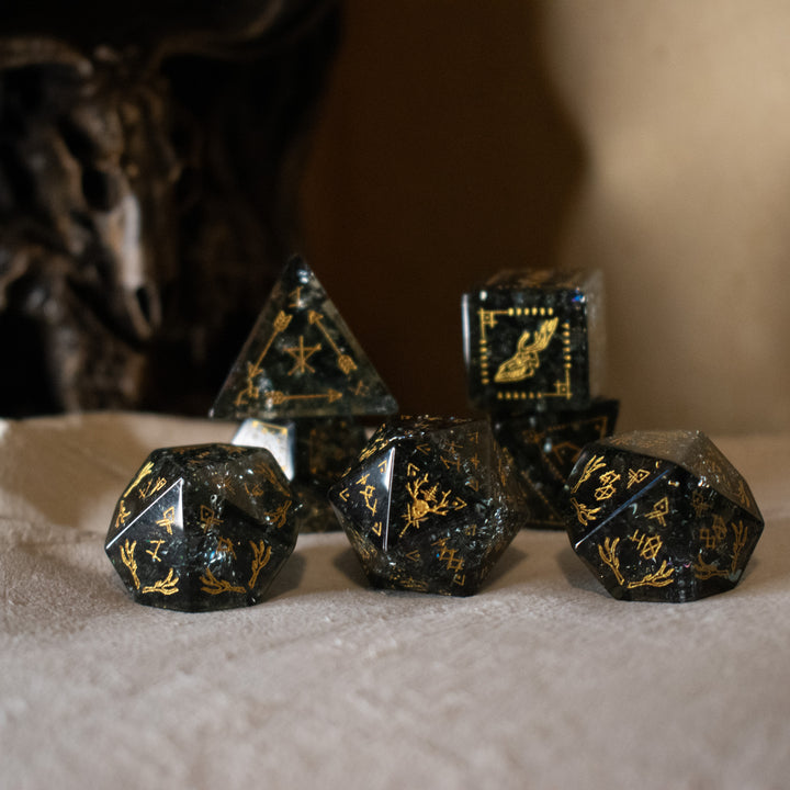 hand-carved, smoky-gray glass dice with gold engraved numbers and wendigo inspired details, displayed against a black background.