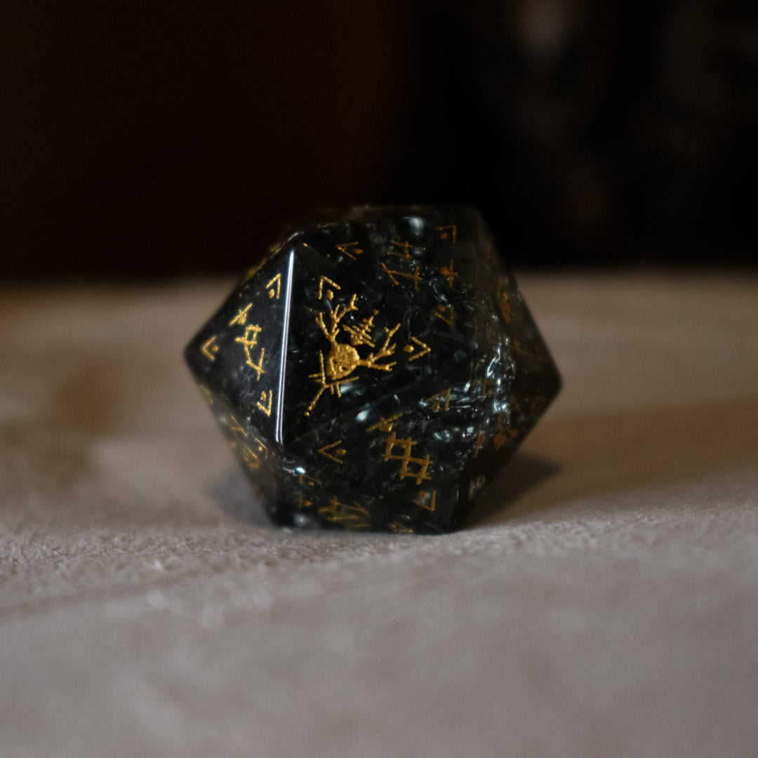 hand-carved, smoky-gray glass dice with gold engraved numbers and wendigo inspired details, displayed against a black background.