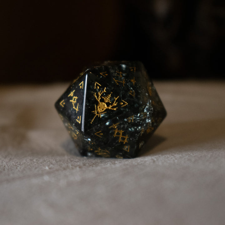 hand-carved, smoky-gray glass dice with gold engraved numbers and wendigo inspired details, displayed against a black background.