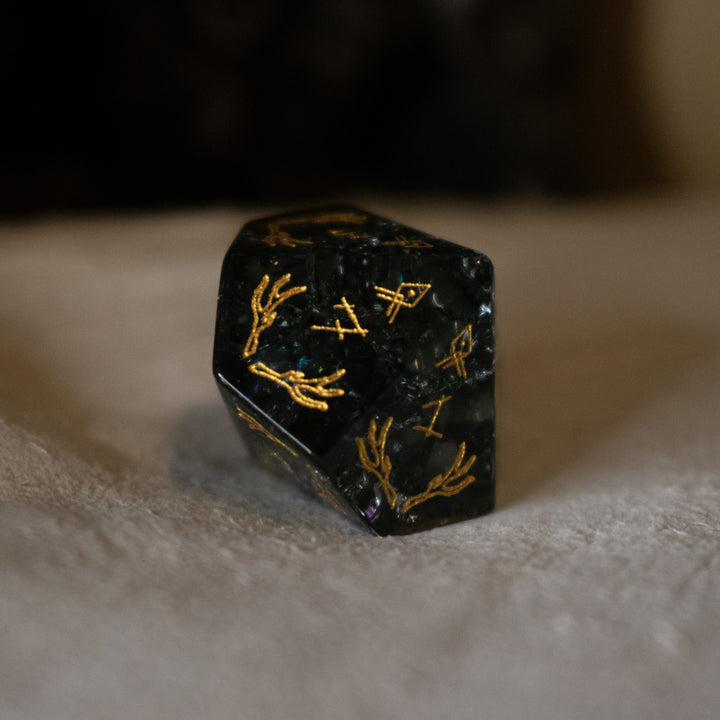 hand-carved, smoky-gray glass dice with gold engraved numbers and wendigo inspired details, displayed against a black background.