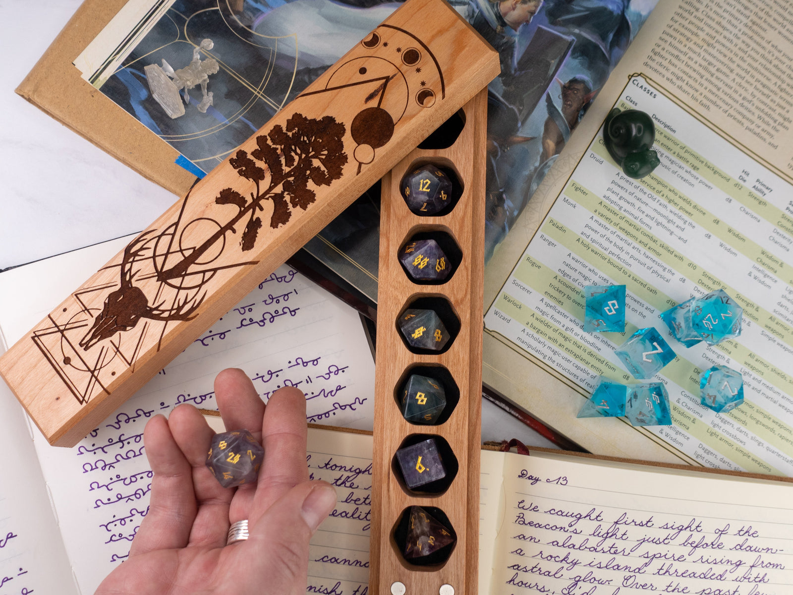 Wooden dice tray with engraved design held by a hand, surrounded by books and dice on a table.