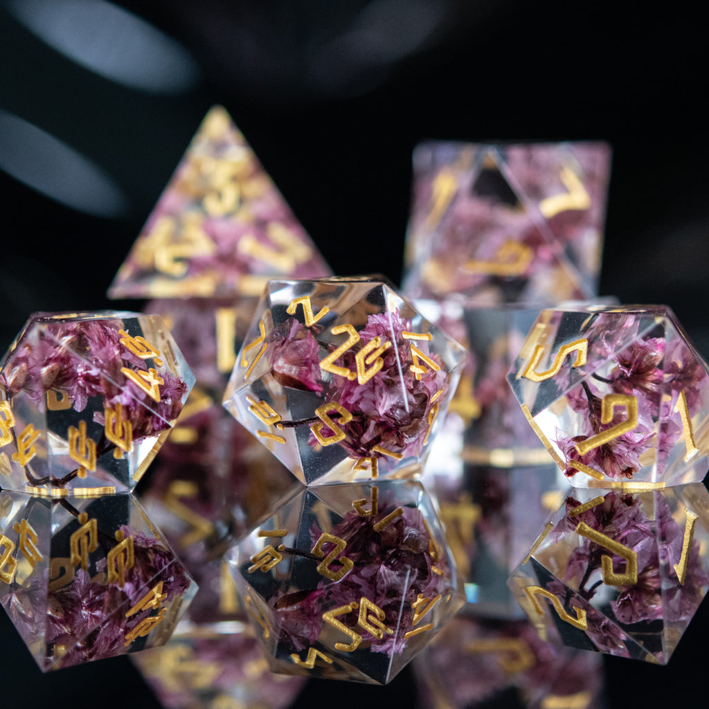 A set of clear sharp-edged resin dice with hand-painted gold numbers, featuring pink florals inside for dungeons and dragons and tabletop gaming