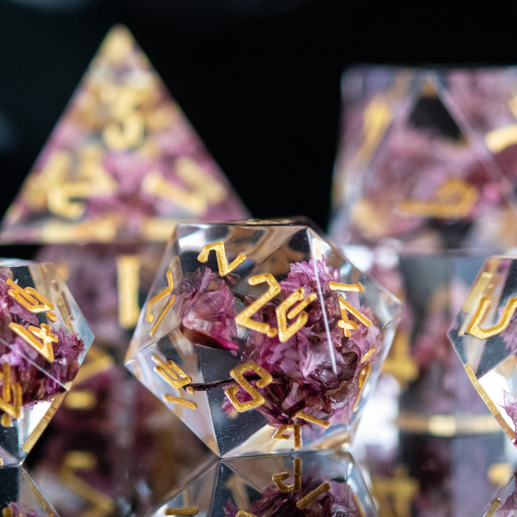 A set of clear sharp-edged resin dice with hand-painted gold numbers, featuring pink florals inside for dungeons and dragons and tabletop gaming