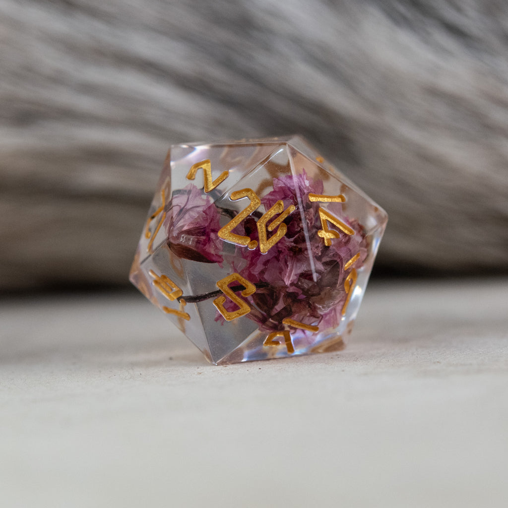 A set of clear sharp-edged resin dice with hand-painted gold numbers, featuring pink florals inside for dungeons and dragons and tabletop gaming
