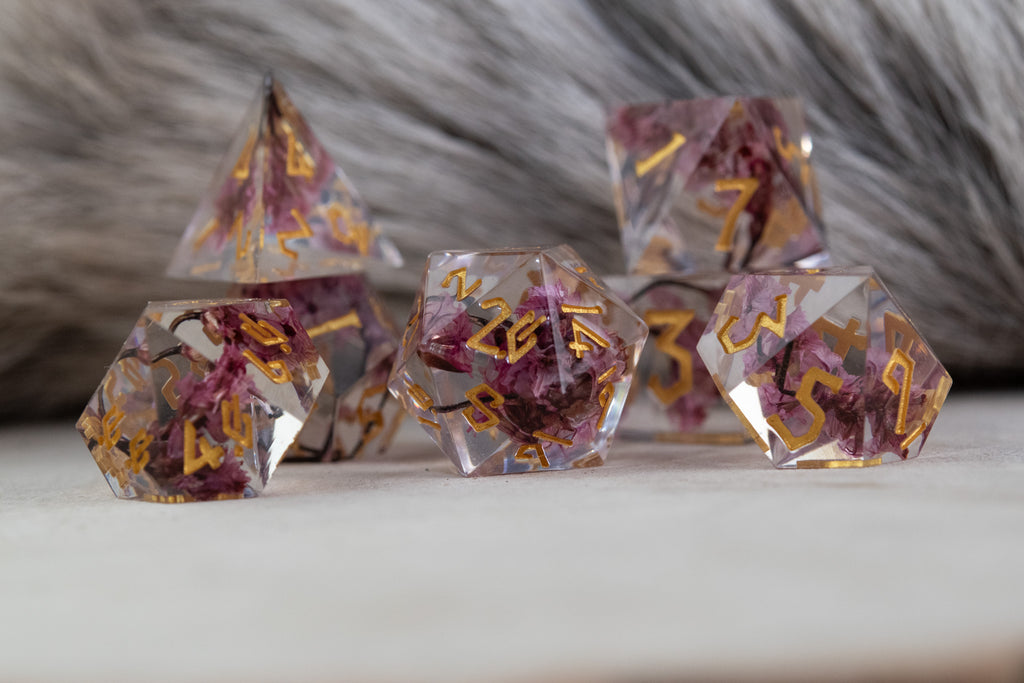 A set of clear sharp-edged resin dice with hand-painted gold numbers, featuring pink florals inside for dungeons and dragons and tabletop gaming