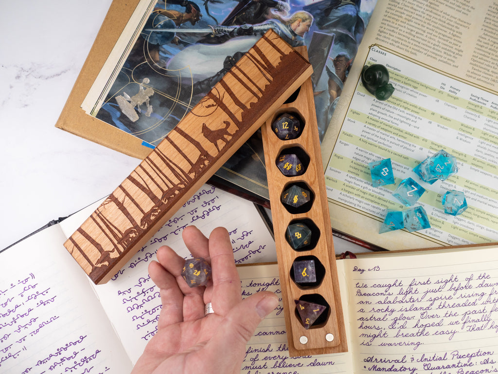 Hand holding polyhedral dice with a wooden dice vault on top of books and game materials.