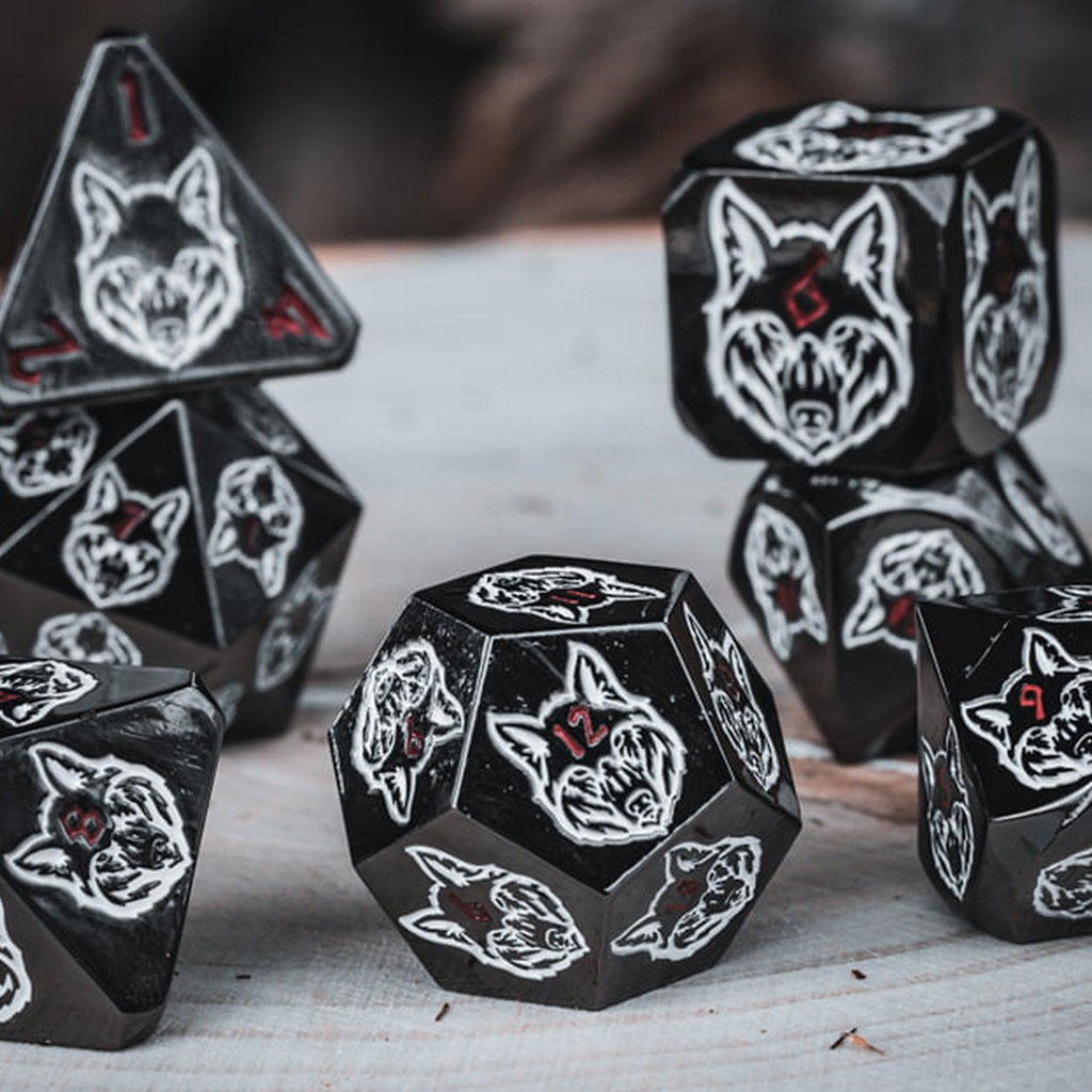 A set of black metal dice with white wolf head designs on each face and red small numbers on a wooden surface