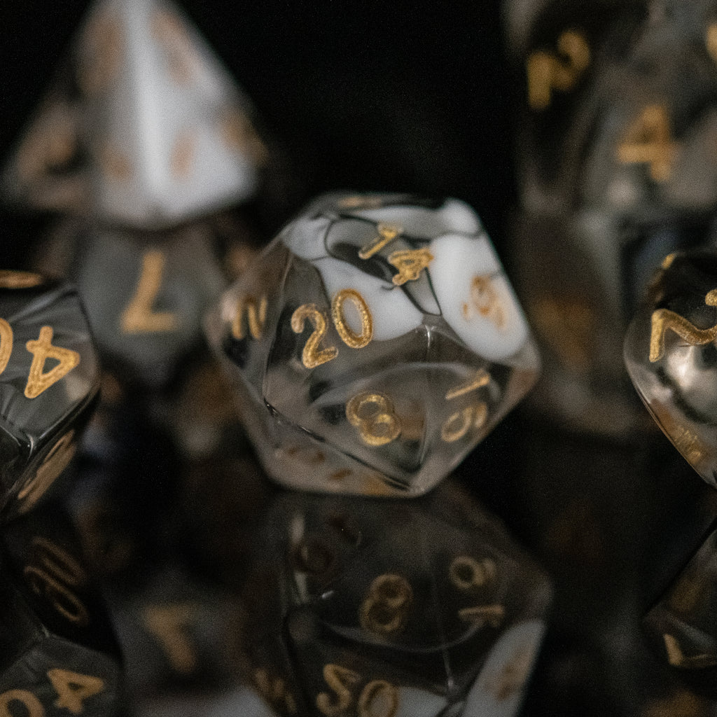 a set of clear acrylic dice with swirls of white and black throughout with gold simple numbering on each die face for dungeons and dragons