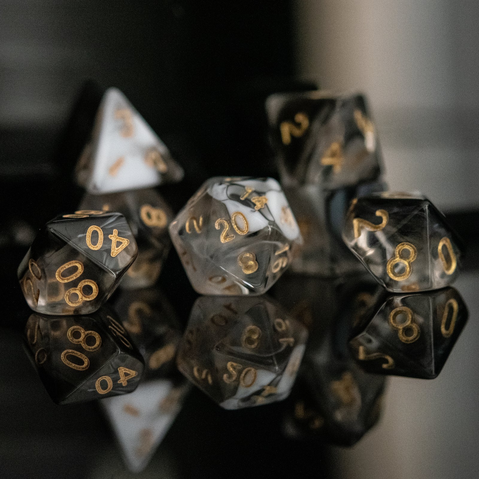 A set of acrylic dice with engraved numbers, featuring black and white colors with gold numbering, displayed on a reflective surface.