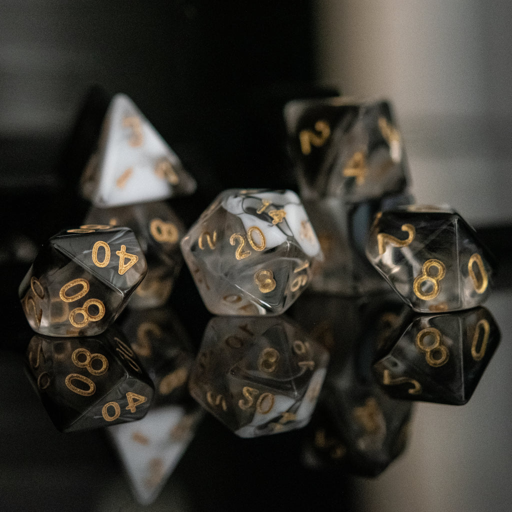 A set of acrylic dice with engraved numbers, featuring black and white colors with gold numbering, displayed on a reflective surface.