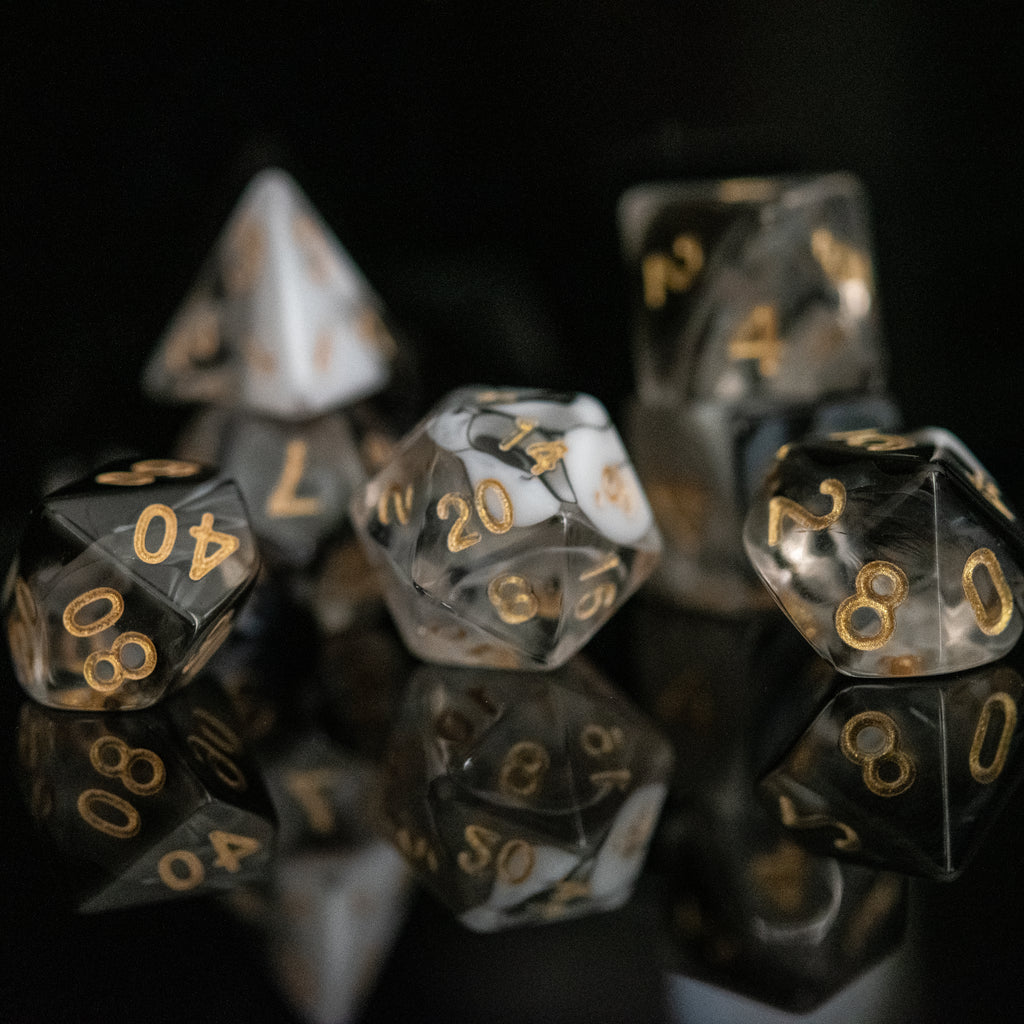 a set of clear acrylic dice with swirls of white and black throughout with gold simple numbering on each die face for dungeons and dragons