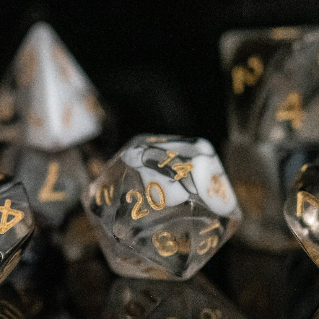A set of acrylic dice with engraved numbers, featuring black and white colors with gold numbering, displayed on a reflective surface.