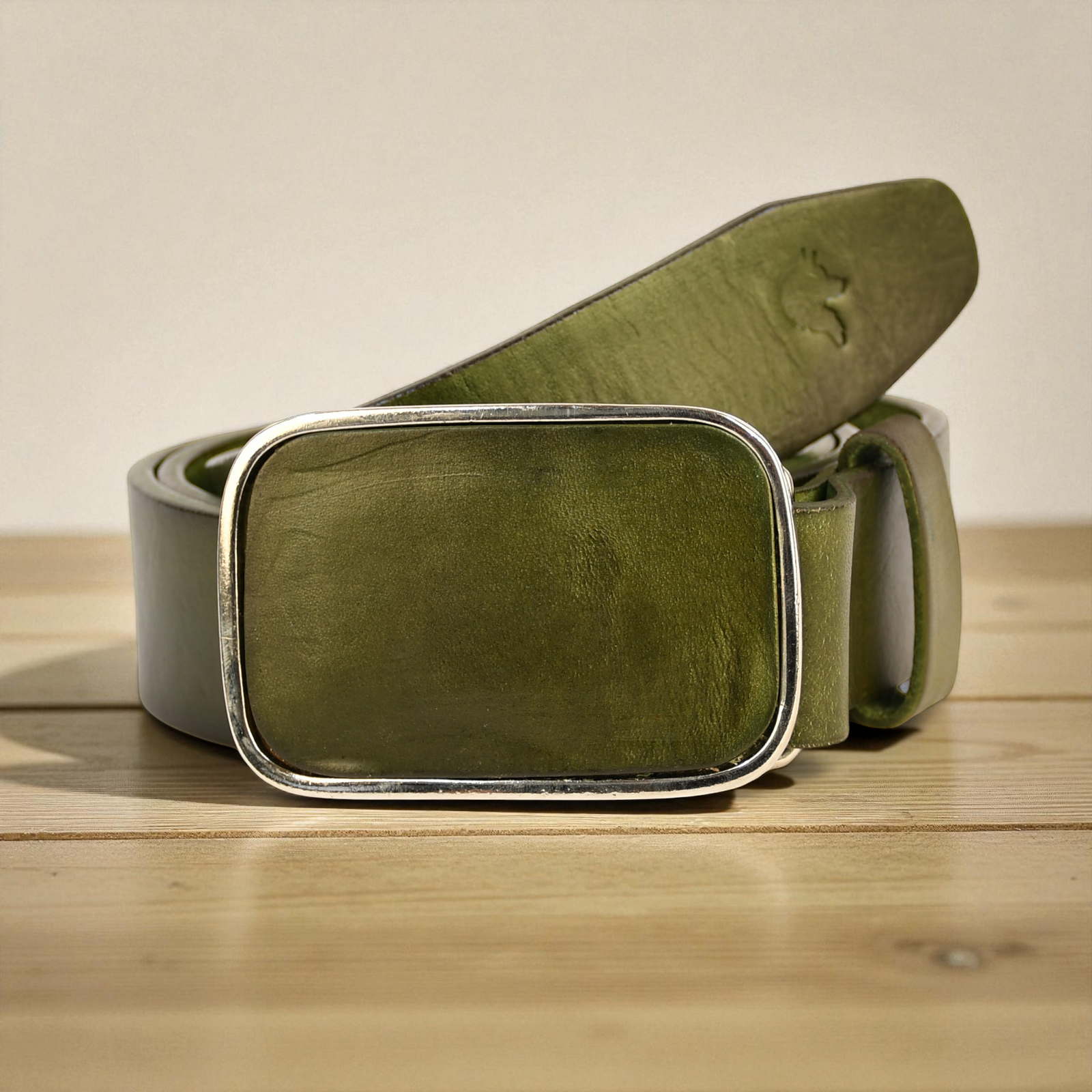 Green leather belt with silver buckle on a wooden surface
