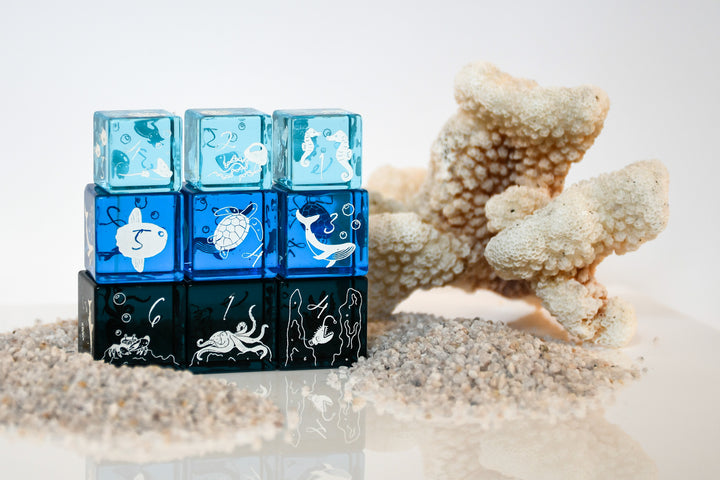 Stack of blue and black cubes with ocean-themed illustrations on a sandy background