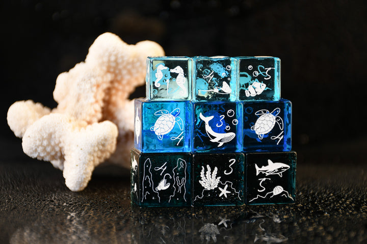 Stack of blue transparent cubes with ocean-themed designs on a dark surface with coral.