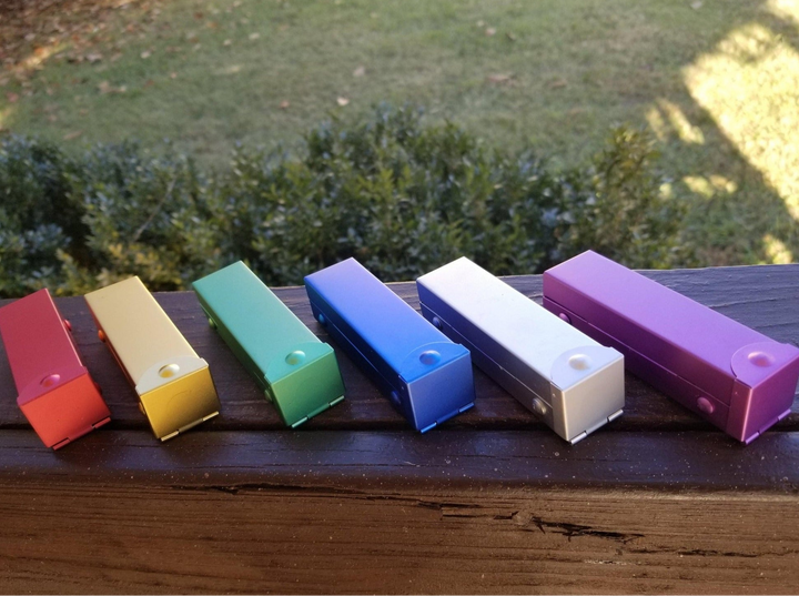 six metal d6 dice cases in red, gold, green, blue, silver and purple