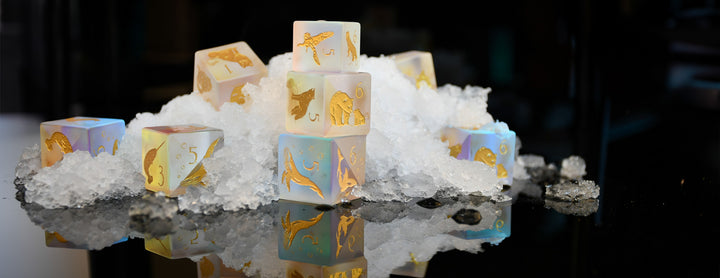 Decorative cubes with gold leaf patterns on a reflective surface with ice cubes.