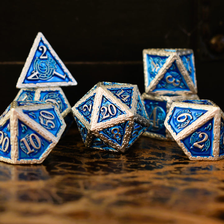 A set of blue and silver metal dice with musical note details around the silver numbers on a wooden surface, including various shapes such as a d4, d6, d8, d10, d12, and d20.