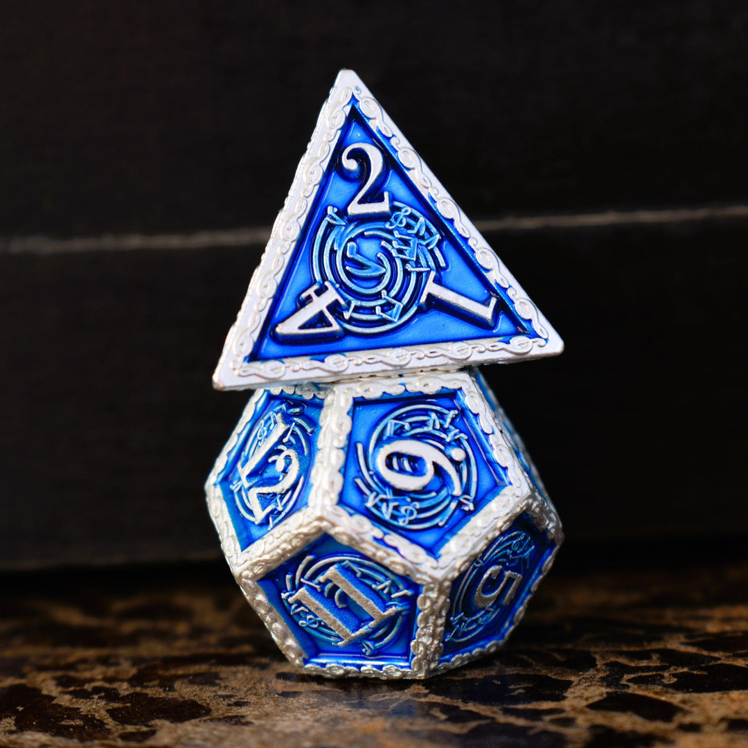 A set of blue and silver metal dice with musical note details around the silver numbers on a wooden surface, including various shapes such as a d4, d6, d8, d10, d12, and d20.