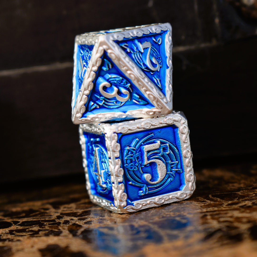 A set of blue and silver metal dice with musical note details around the silver numbers on a wooden surface, including various shapes such as a d4, d6, d8, d10, d12, and d20.