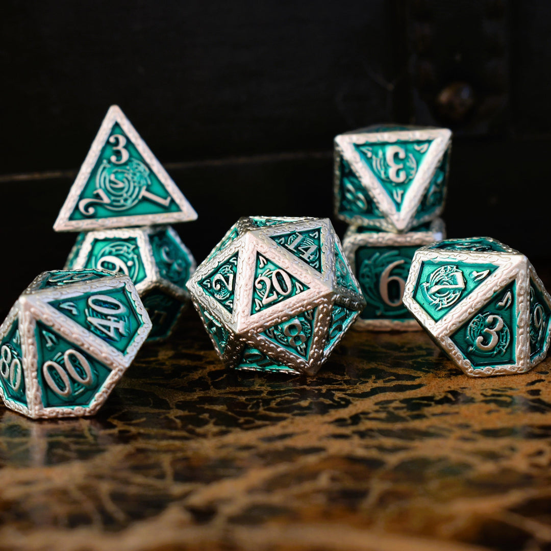 A set of green and silver metal dice with musical note details around the silver numbers on a wooden surface, including various shapes such as a d4, d6, d8, d10, d12, and d20.