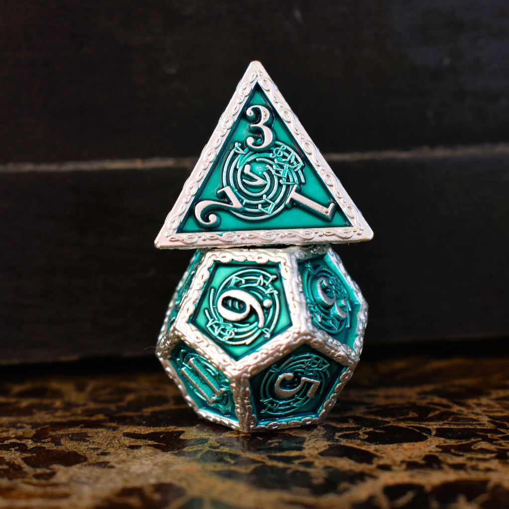 A set of green and silver metal dice with musical note details around the silver numbers on a wooden surface, including various shapes such as a d4, d6, d8, d10, d12, and d20.