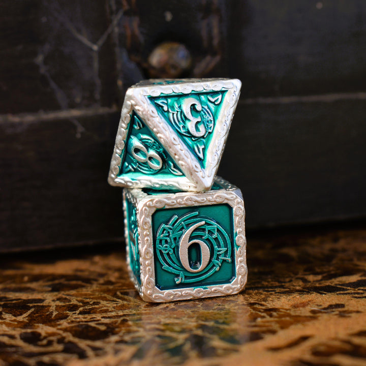 A set of green and silver metal dice with musical note details around the silver numbers on a wooden surface, including various shapes such as a d4, d6, d8, d10, d12, and d20.