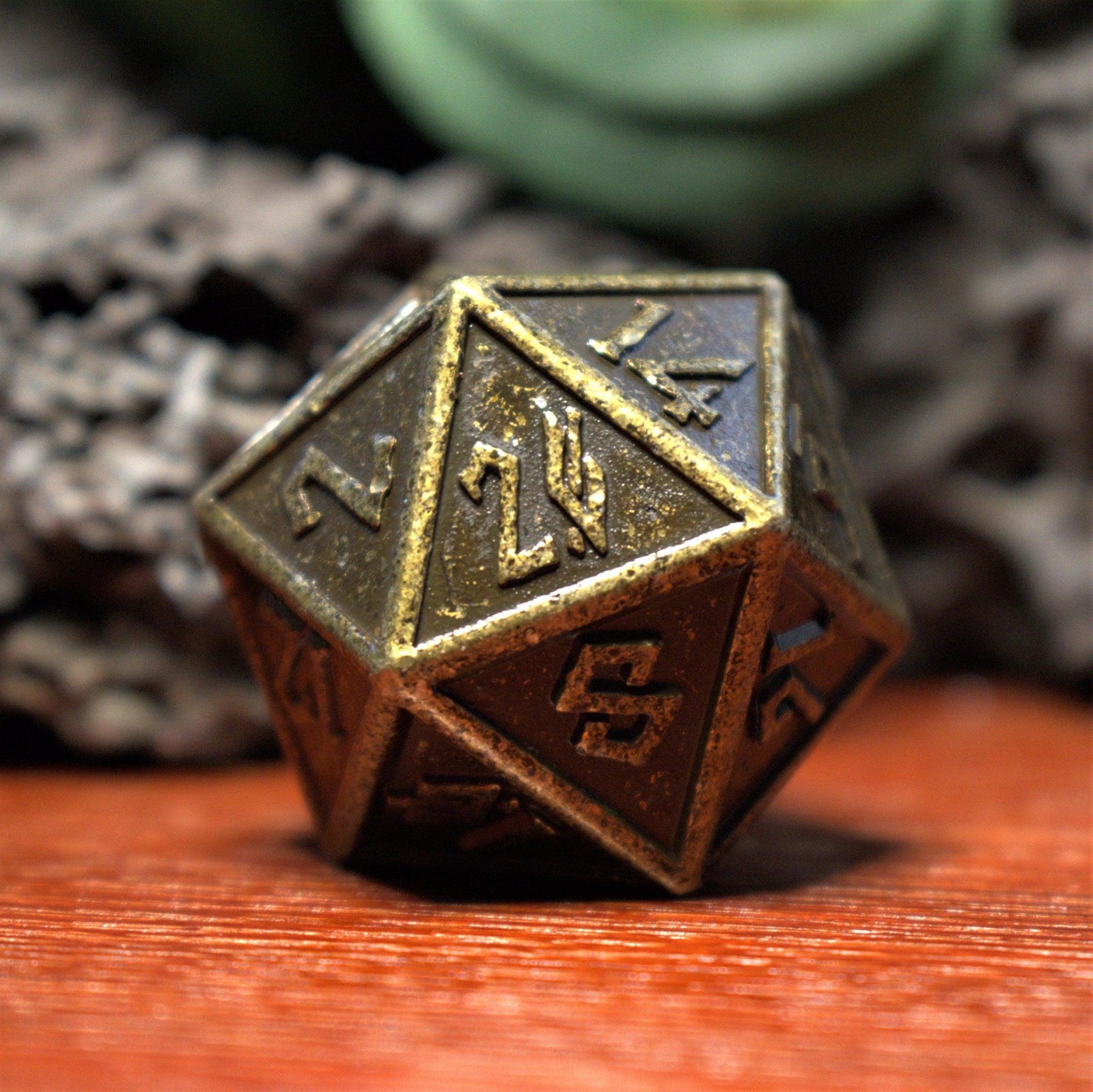 A close-up of a bronze-colored metal D20 dice with embossed numbers, placed on a wooden surface.